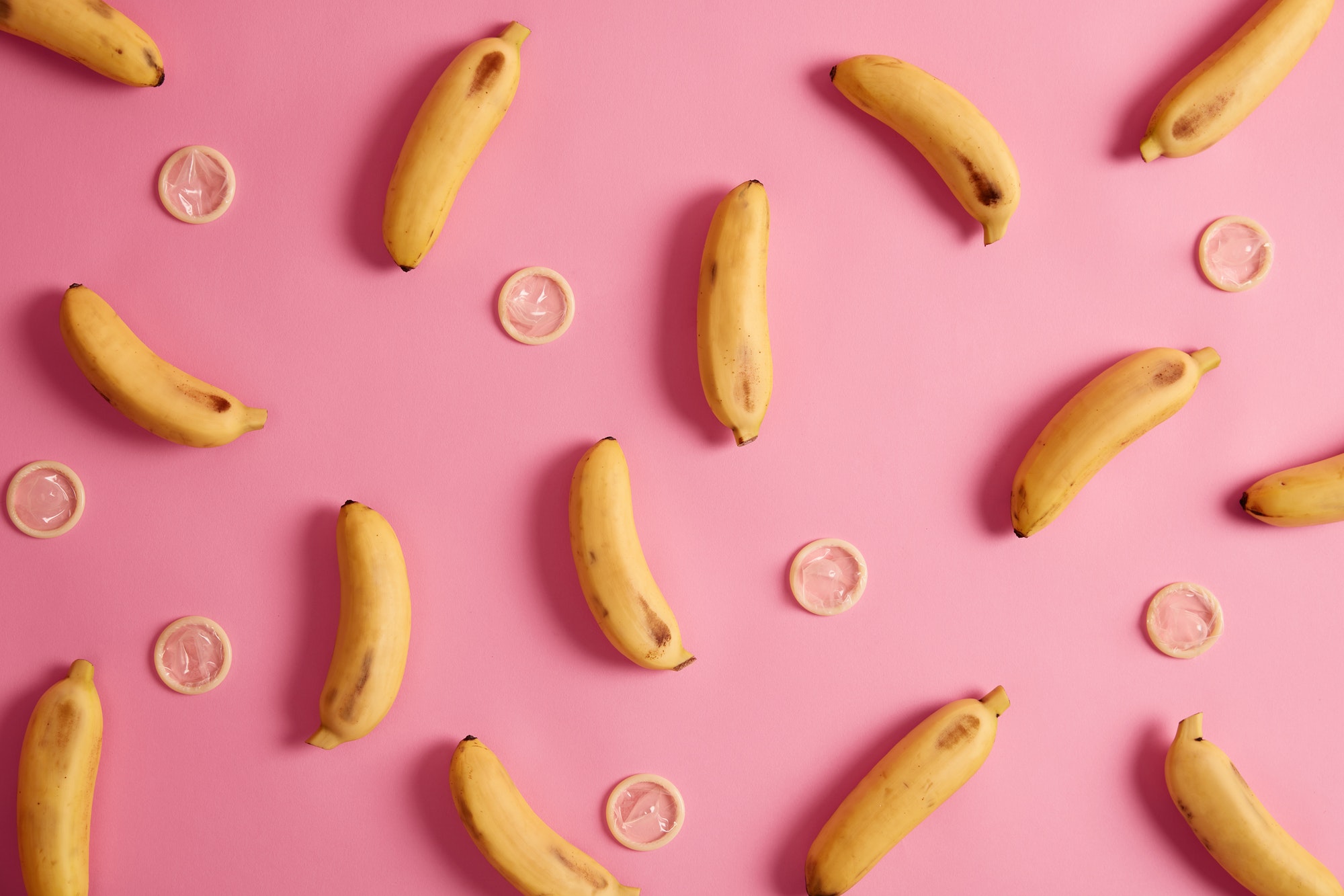 Bananas and contraceptives on pink background. Tropical flavored condom for safe relationship. Elimi