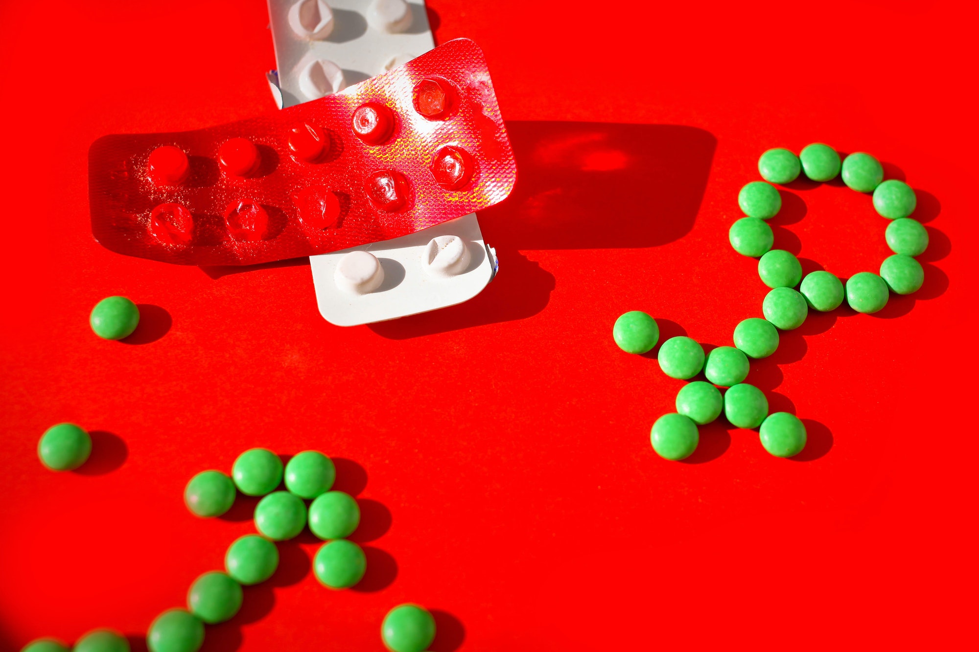 Gender symbol made from green pills or tablets on a red background.