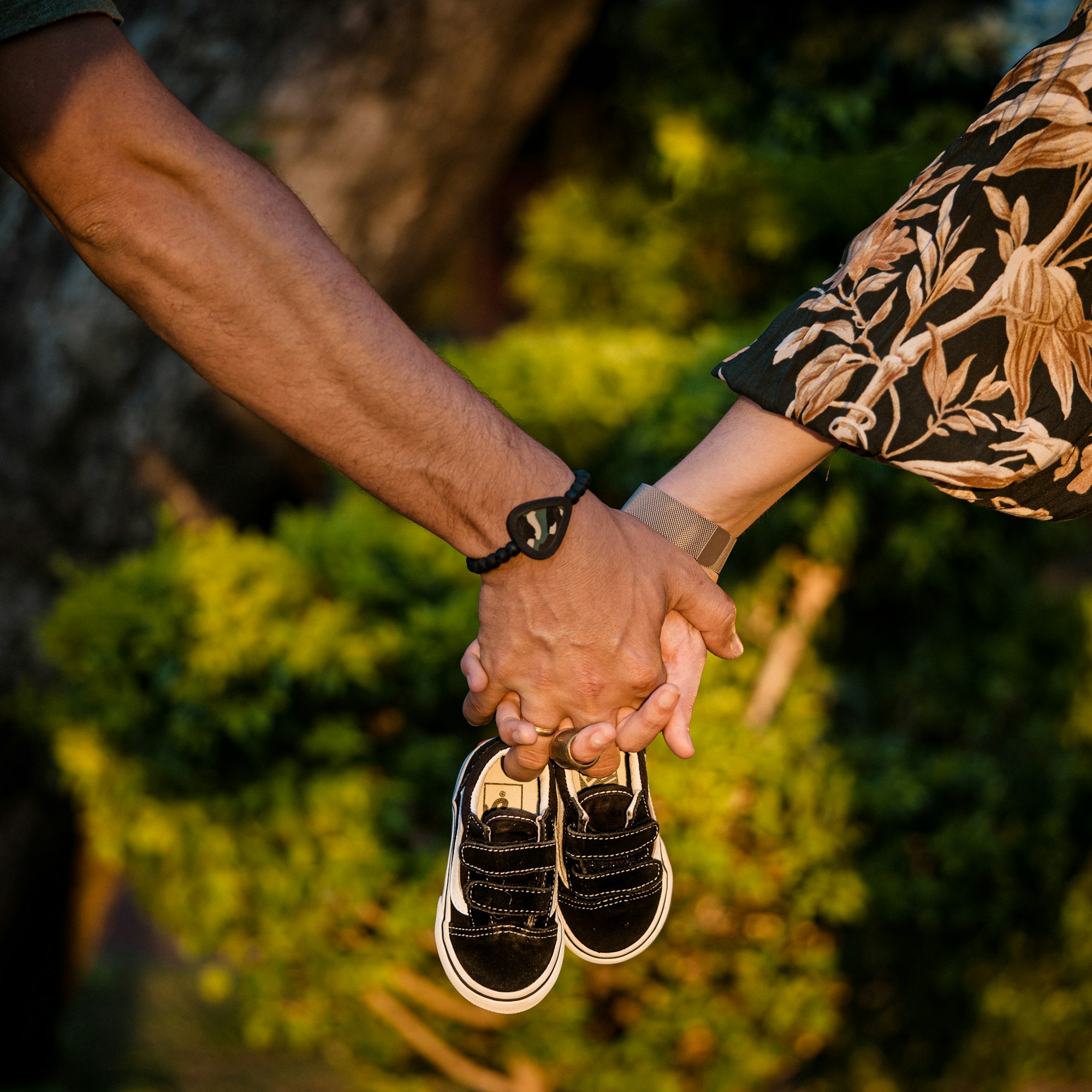 parents holding hands holding baby shoes on a sunny sunset