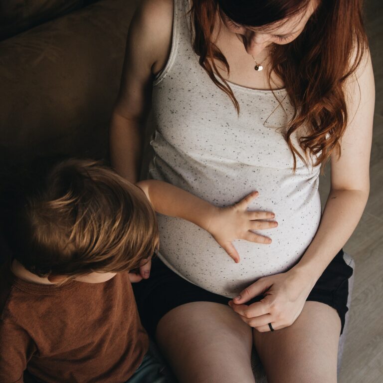 Toddler boy touching the belly of his pregnant mother in the living room of their home